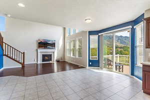 Unfurnished living room featuring a textured ceiling, light tile patterned floors, a tiled fireplace, and stairway