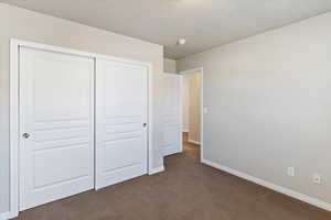 Unfurnished bedroom featuring dark carpet, a textured ceiling, and a closet