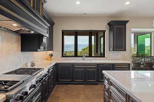 Kitchen featuring custom exhaust hood, recessed lighting, stainless steel gas cooktop, light stone countertops, and a mountain view