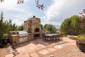 View of patio / terrace featuring area for grilling, outdoor dining space, a mountain view, and an outdoor stone fireplace