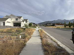 View of asphalt road with sidewalks, a mountain view, a residential view, and curbs