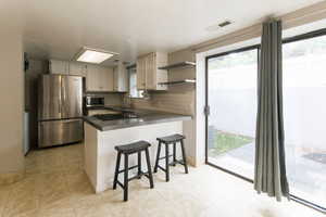 Kitchen with open shelves, appliances with stainless steel finishes, backsplash, dark countertops, and a peninsula