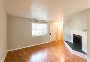 Unfurnished living room featuring wood finished floors, a brick fireplace, and a textured ceiling