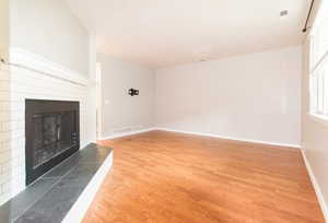 Unfurnished living room with light wood-style flooring and a fireplace with raised hearth