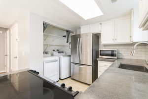 Kitchen featuring appliances with stainless steel finishes, white cabinetry, decorative backsplash, separate washer and dryer, and light tile patterned flooring