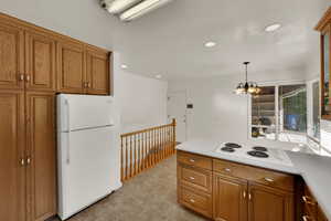 Kitchen featuring brown cabinets, white appliances, pendant lighting, light countertops, and recessed lighting