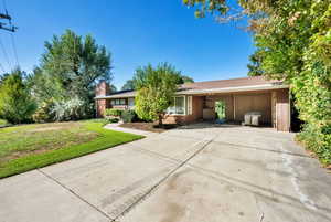 Ranch-style house with driveway, a front lawn, a chimney, and brick siding