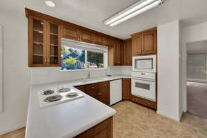 Kitchen featuring light countertops, brown cabinets, white appliances, glass insert cabinets, and backsplash