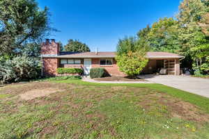 Ranch-style home featuring a chimney, concrete driveway, a front yard, brick siding, and an attached carport