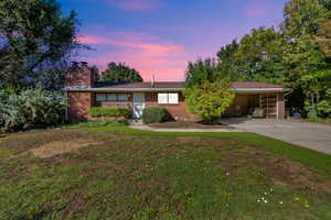 Single story home featuring driveway, a yard, a chimney, and brick siding