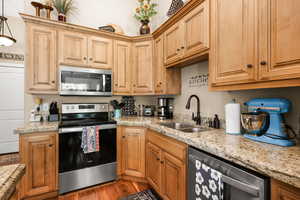 Kitchen featuring stainless steel appliances, light stone countertops, wood finished floors, and pendant lighting