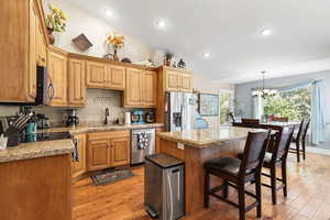 Kitchen with a center island, light stone countertops, appliances with stainless steel finishes, light wood-style flooring, and decorative light fixtures