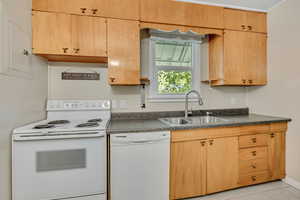 Kitchen featuring white appliances, dark countertops, electric panel, light brown cabinetry, and light tile patterned floors