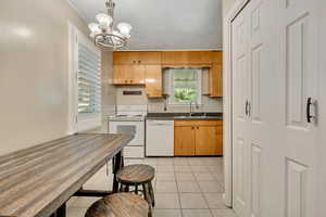 Kitchen with white appliances, light tile patterned floors, decorative light fixtures, a chandelier, and dark stone counters