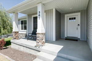 Doorway to property featuring covered porch, board and batten siding, and stone siding