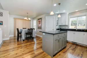 Kitchen with gray cabinets, hanging light fixtures, a center island, dark stone countertops, and light wood finished floors
