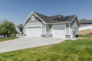View of front of house with roof mounted solar panels, an attached garage, driveway, stone siding, and a front yard
