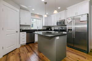 Kitchen featuring appliances with stainless steel finishes, pendant lighting, a center island, dark stone countertops, and dark wood-style flooring