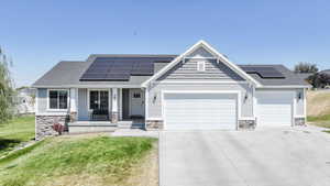 View of front facade with stone siding, roof mounted solar panels, a garage, driveway, and a porch