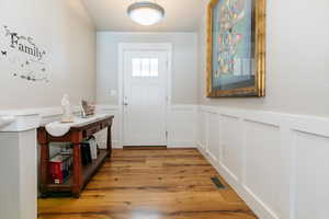 Doorway to outside with a wainscoted wall, wood finished floors, and a decorative wall