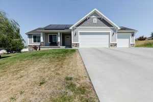 Craftsman inspired home with solar panels, stone siding, a garage, and a porch