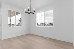 Spare room with healthy amount of natural light, light wood-type flooring, and a chandelier