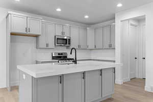 Kitchen with tasteful backsplash, gray cabinets, light wood finished floors, recessed lighting, and stainless steel appliances
