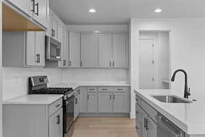 Kitchen featuring stainless steel appliances, gray cabinets, recessed lighting, light wood finished floors, and light stone countertops