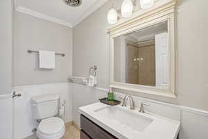 Full bath featuring wainscoting, ornamental molding, vanity, a decorative wall, and a shower