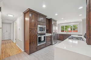 Kitchen with ornamental molding, stainless steel appliances, recessed lighting, light countertops, and dark brown cabinets