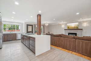 Kitchen with crown molding, open floor plan, light countertops, recessed lighting, and a tiled fireplace