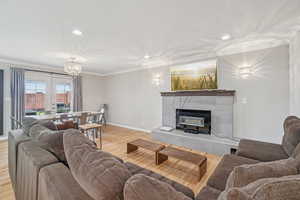 Living room with ornamental molding, wood finished floors, a fireplace, recessed lighting, and a chandelier