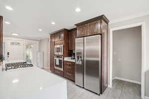 Kitchen with stainless steel appliances, ornamental molding, light countertops, dark brown cabinetry, and recessed lighting
