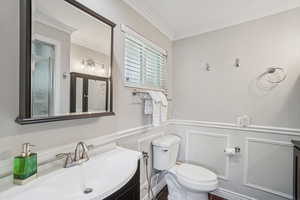 Bathroom with crown molding, vanity, a decorative wall, and a wainscoted wall