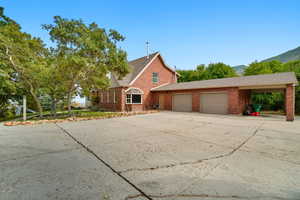 View of side of property with brick siding, concrete driveway, a mountain view, roof with shingles, and an attached garage