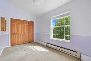 Unfurnished bedroom with a baseboard heating unit, light colored carpet, lofted ceiling, a closet, and a ceiling fan