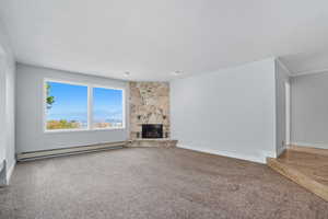 Unfurnished living room with a baseboard heating unit, a stone fireplace, light carpet, a textured ceiling, and a mountain view