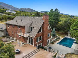 Rear view of property with a chimney, brick siding, an outdoor pool, roof with shingles, and a deck with mountain view