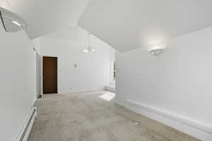 Spare room featuring a chandelier, a baseboard radiator, light carpet, and high vaulted ceiling