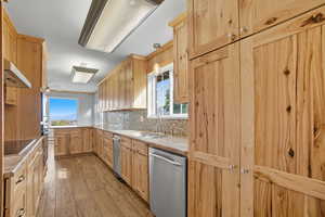 Kitchen featuring light brown cabinets, decorative backsplash, a peninsula, appliances with stainless steel finishes, and hanging light fixtures