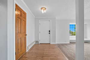 Entryway featuring light wood-style floors, a textured ceiling, ornamental molding, a baseboard radiator, and light colored carpet