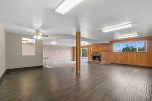 Unfurnished living room with dark wood-type flooring, a brick fireplace, a textured ceiling, a ceiling fan, and baseboard heating