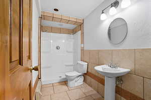 Bathroom featuring tile walls, a shower stall, tile patterned floors, and a textured wall