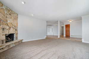 Unfurnished living room with a stone fireplace, carpet floors, and baseboard heating