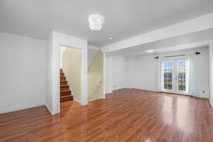 Unfurnished room with wood finished floors, french doors, and stairs
