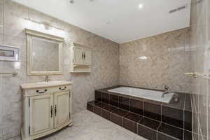 Full bathroom with tile walls, vanity, a bath, and light tile patterned flooring
