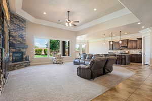 Living room with a raised ceiling, recessed lighting, a fireplace, a ceiling fan, and crown molding