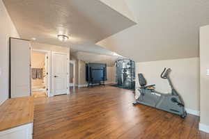 Workout area featuring a textured ceiling, hardwood / wood-style floors, and lofted ceiling