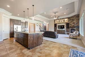 Kitchen featuring dark brown cabinetry, a fireplace, pendant lighting, ceiling fan, and open floor plan