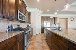 Kitchen with stainless steel appliances, dark brown cabinets, a textured ceiling, light stone counters, and decorative light fixtures